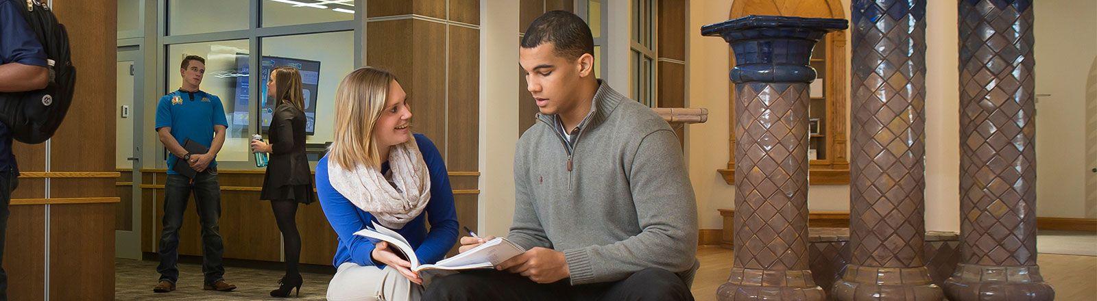 Two students sitting in lobby of Kepner Hall looking at book